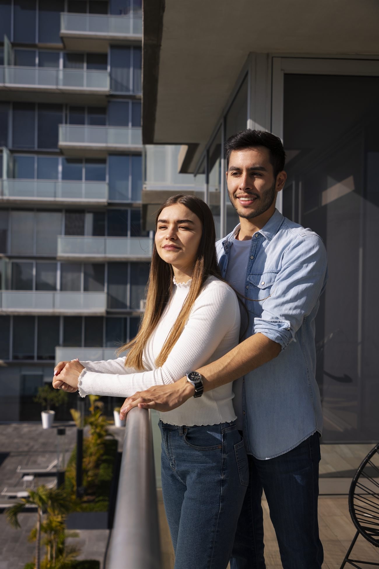 Casal jovem na varanda de um apartamento em dia ensolarado